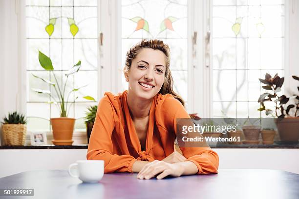 portrait of smiling young woman sitting at blue table at home - woman leaning stock pictures, royalty-free photos & images