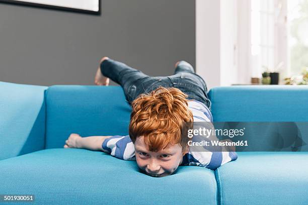 boy rollicking around on blue couch in living room - irreverent stock-fotos und bilder