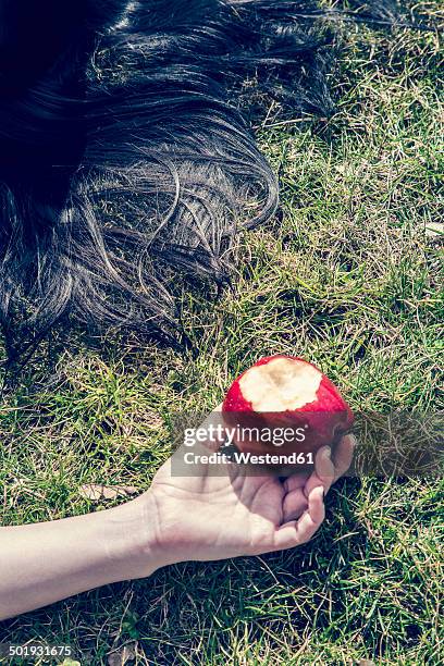 hand of woman lying on grass holding bitten red apple - schneewittchen stock-fotos und bilder