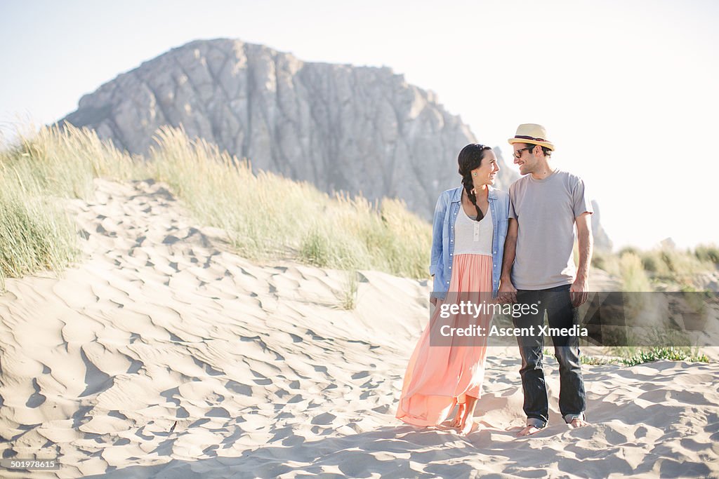 Couple walk through sand dunes, at beach