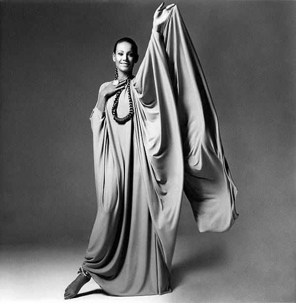 French actress Claudine Auger wearing a long, full, toga-style dress by Stavropoulos, her hair braided in a loop that falls like a necklace, one arm...