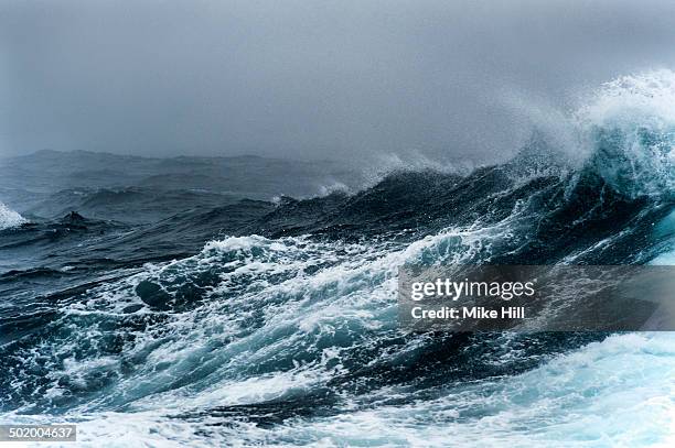 breaking wave on a rough sea against overcast sky - tormenta foto e immagini stock