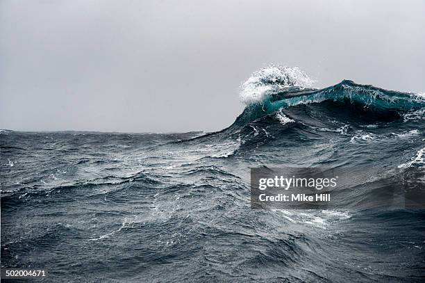 breaking wave on a rough sea against overcast sky - mare tempesta foto e immagini stock