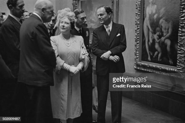 King George VI talking to Sir Kenneth Clarke , director of the National Gallery, while Queen Elizabeth talks to British economist John Maynard Keynes...