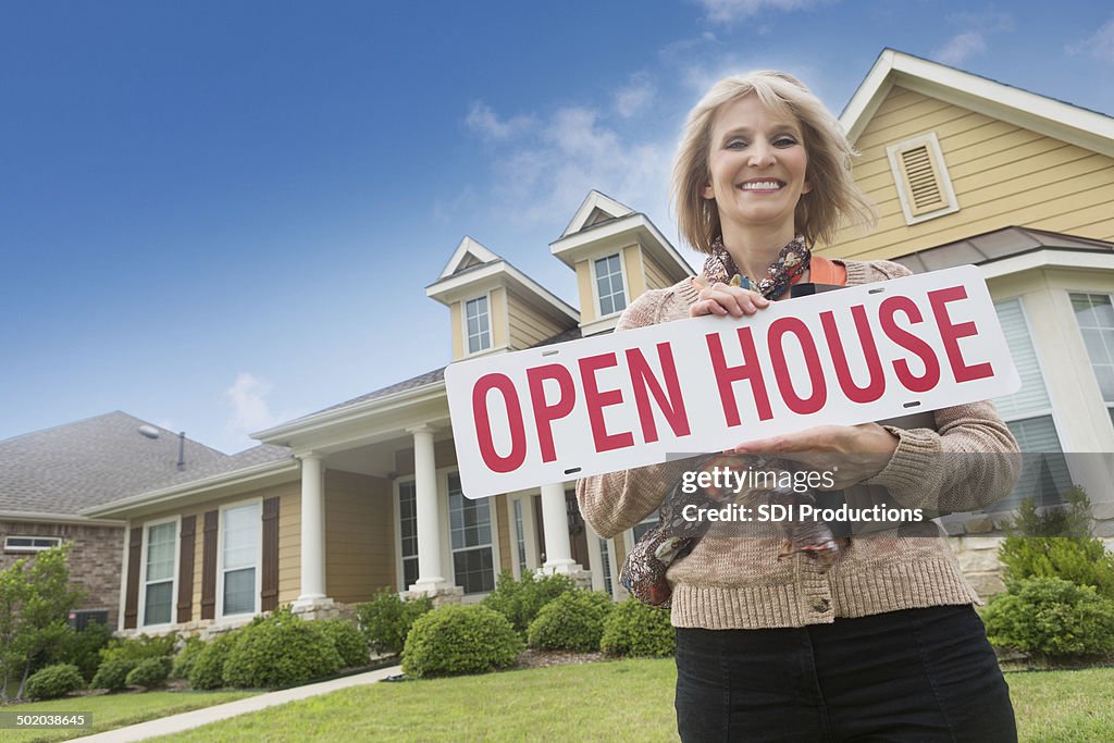 Mature Real Estate Agent holding open house"" sign in front yard