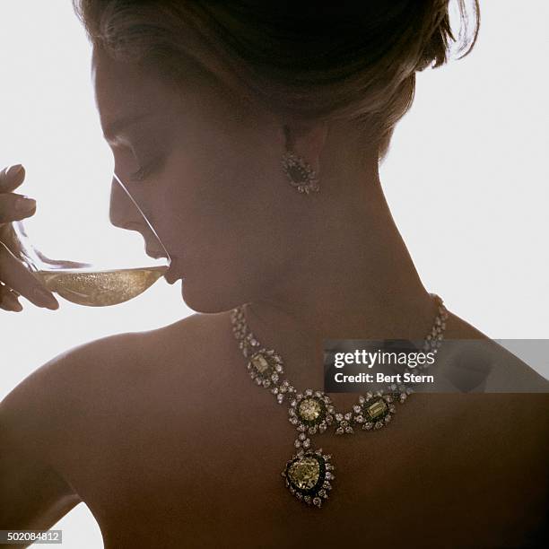 Model wearing a Van Cleef & Arpels necklace of canary diamonds, emeralds, and white diamonds and earrings of emeralds and diamonds drinking wine.