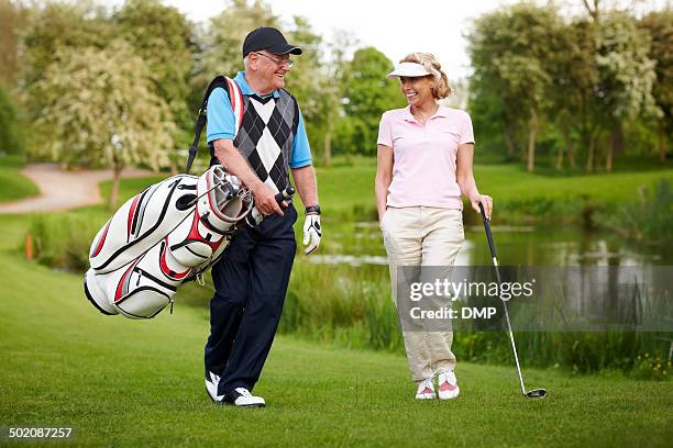 senior couple playing golf walking down the course - senior men golf stock pictures, royalty-free photos & images