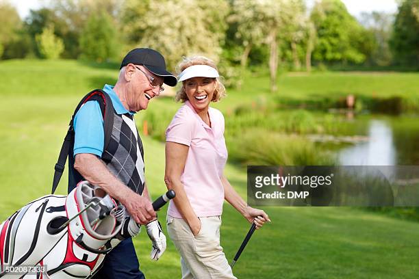 cheerful mature couple walking on a golf course - golf bag stock pictures, royalty-free photos & images