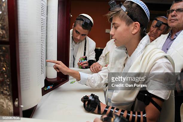 During his Bar Mitzvah ceremony, a boy reads from a Torah scroll, Jerusalem, Israel, November 5, 2015. He wears a Tallit and a set of Tefillin on his...