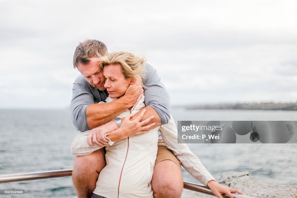 Couple hugging on a railing near an ocean