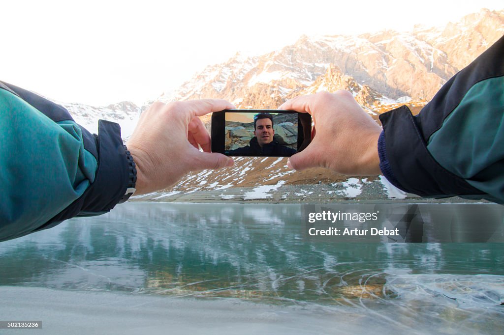 Hiker in the Gran Paradiso national park taking a selfie from point of view with the frozen lake with beautiful reflection on sunset .