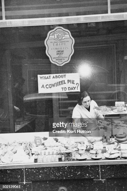 Woman working on a tripe stall in Wigan, Lancashire, November 1939. A sign asks: 'What about a cow-heel pie today?'. Original publication: Picture...
