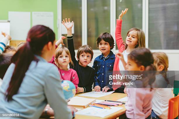 preschool teacher and children with hands raised in classroom. - answering stock pictures, royalty-free photos & images