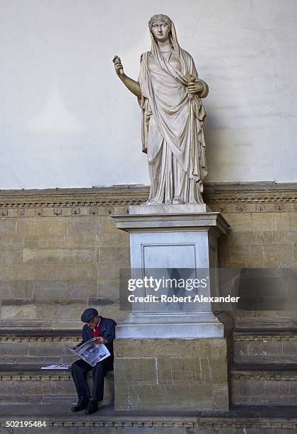 An Italian man reads a newspaper as he sits beside a 2nd century Roman statue of a lady, or 'Sabina,' on display in the Loggia dei Lanzi in Florence,...