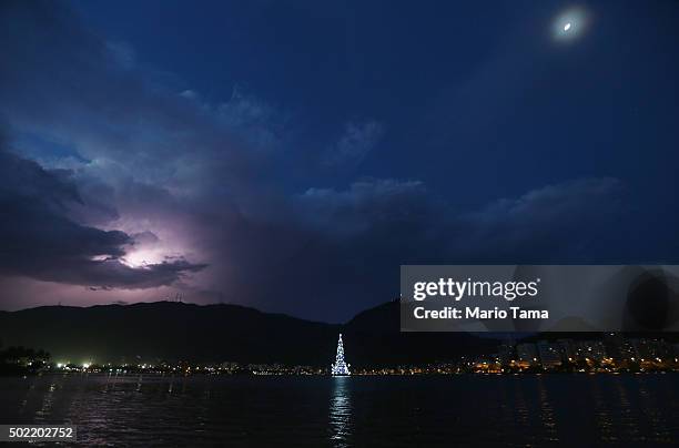 Lightning illuminates a cloud above the floating Christmas tree in the Rodrigo de Freitas lagoon, with the moon at top right, on December 21, 2015 in...