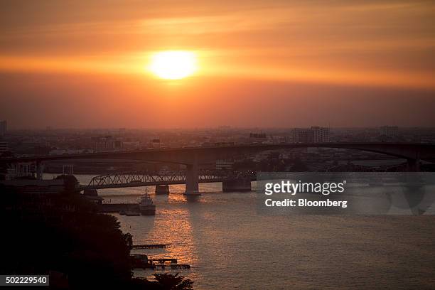 The sun setting over the Rama III bridge, front, and the Bangkok bridge on the Chao Phraya is seen through the window of a passenger pod on the...
