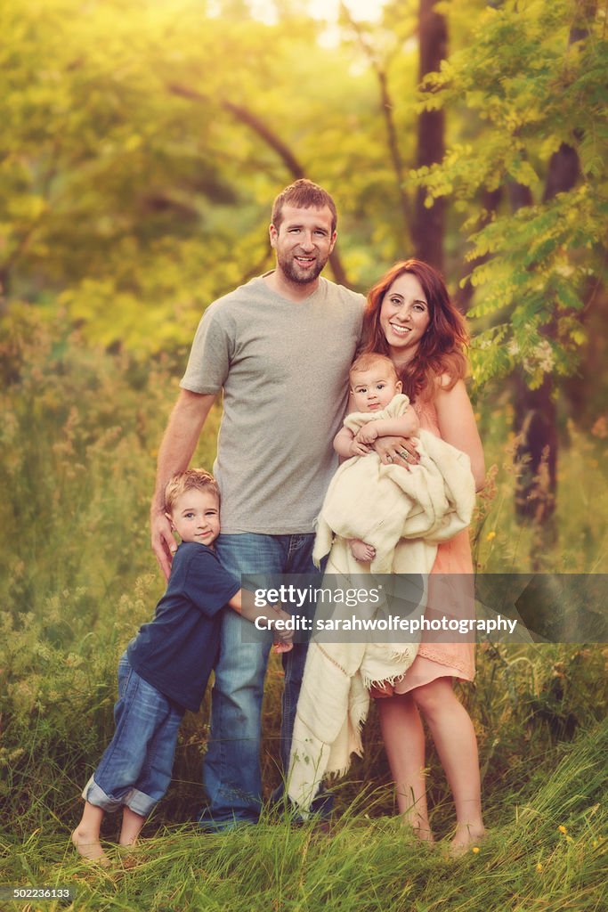 Family of four standing in green forest