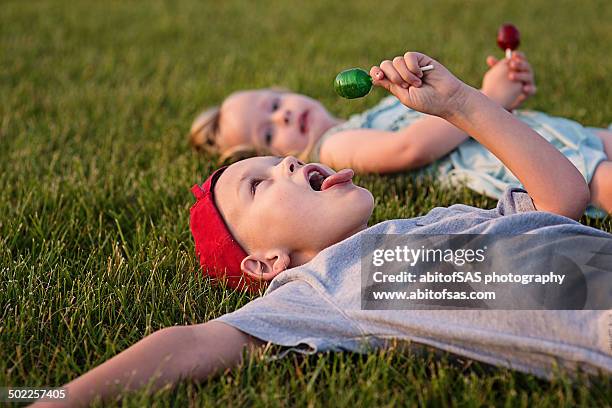 siblings laying on grass with lollipops - lollipop boys stock pictures, royalty-free photos & images