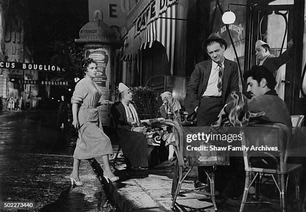 Italian actress Gina Lollabrigida approaches Sid James at an outdoor cafe busy with performers and clowns in 1955 during the filming of 'Trapeze' in...