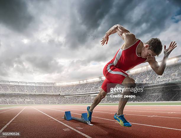 elite 100m runner sprints from blocks in floodlit stadium - sports race stock pictures, royalty-free photos & images