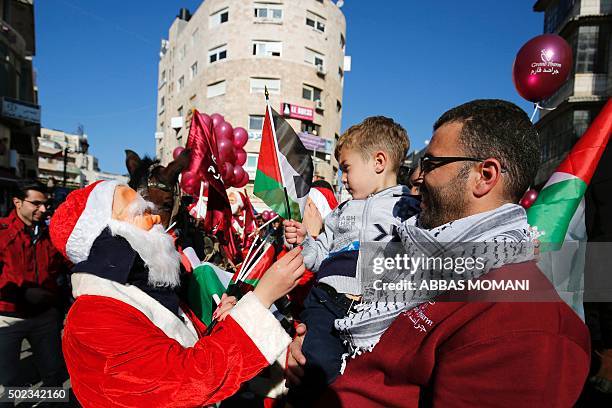 Palestinian dressed up as Santa Claus distributes Palestinian flags to people on a street in the West Bank city of Ramallah, on December 23, 2015 as...