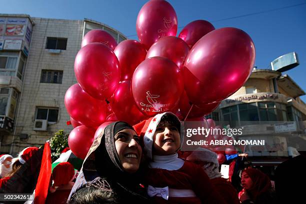 Palestinians watch people dressed up as Santa Claus distributing gifts on a street in the West Bank city of Ramallah, on December 23, 2015 as...