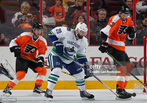 Chris Higgins of the Vancouver Canucks battles for control of the puck against Brandon Manning and Shayne Gostisbehere of the Philadelphia Flyers on...