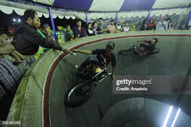 Performer drives a motorcycle and catches the money from a visitor on the Wall of Death at the night market in Surakarta, Central Java, Indonesia, on...