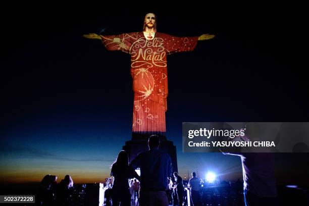 People take pictures of the statue of Christ the Redeemer illuminated by Brazil-based French lighting designer Gaspare Di Caro reading "Merry...