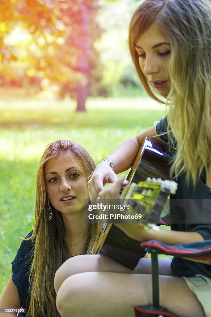 Two young women relaxing playing guitar