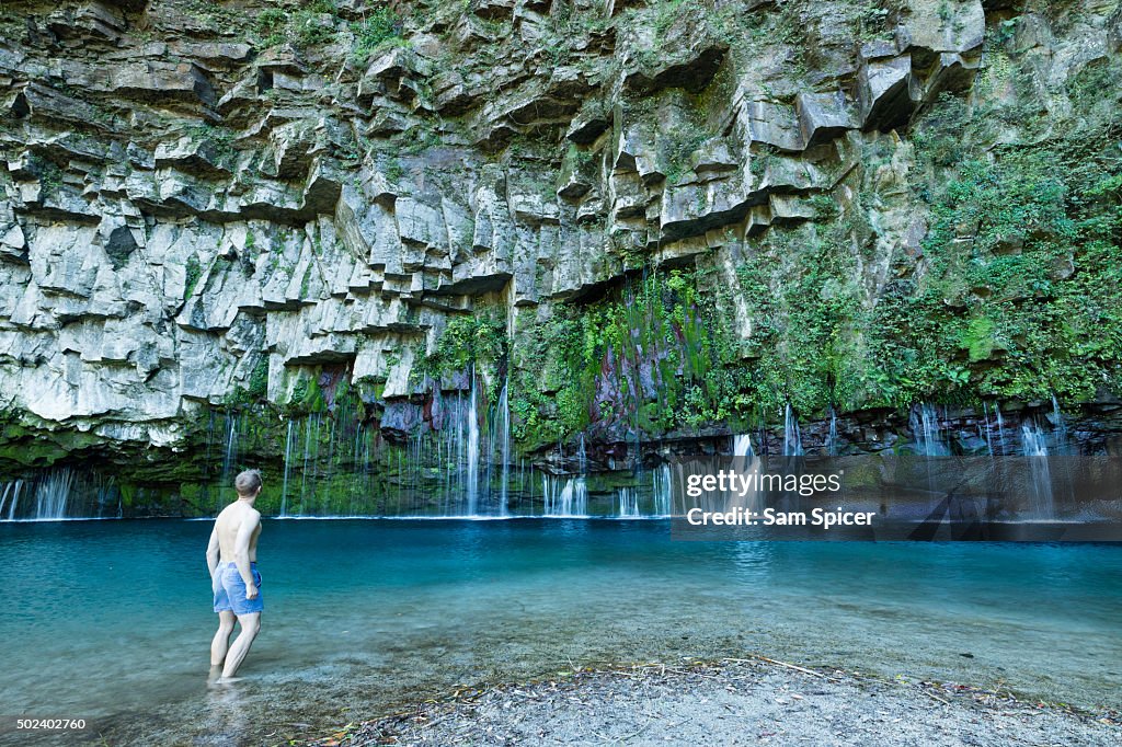 Man looking at stunning waterfall with columnar jointed basalt rocks and clear turquoise lagoon water, Kyushu, Japan