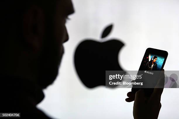 Man checks the Apple Music streaming site using his Apple Inc. IPhone 6s as he stands framed against a wall bearing the Apple logo in this arranged...