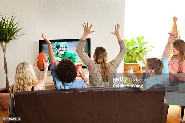 group of friends watching and cheering football game together - american football speler stockfoto's en -beelden