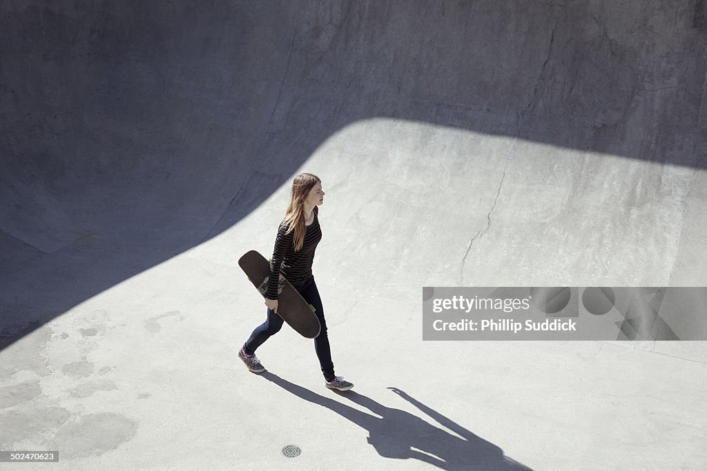 Girl skateboarder walking through a concrete bowl