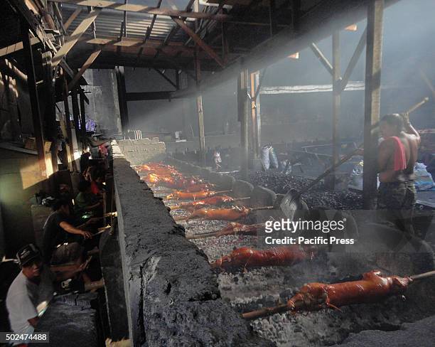 Filipino worker places coal as workers handle roasted pig cooked in bamboo rotiserries at suburban Quezon City, east of Manila, Philippines. Roasted...