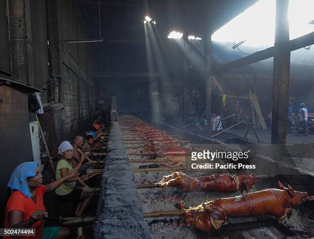 Filipino workers handle roasted pig cooked in bamboo rotiserries at suburban Quezon City, east of Manila, Philippines. Roasted pig, locally called...