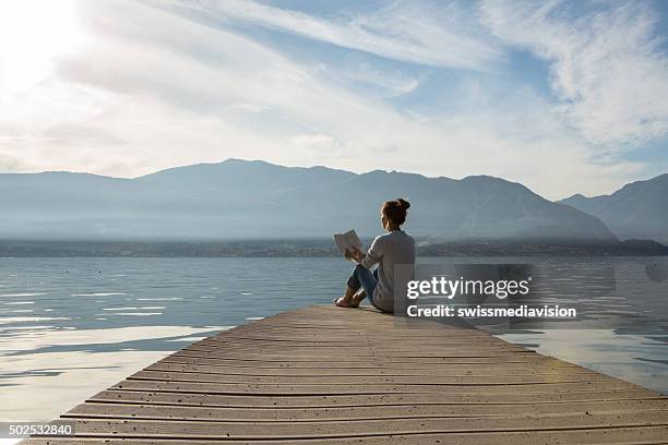 woman relaxes on lake pier, reads a book - jetty lake stock pictures, royalty-free photos & images