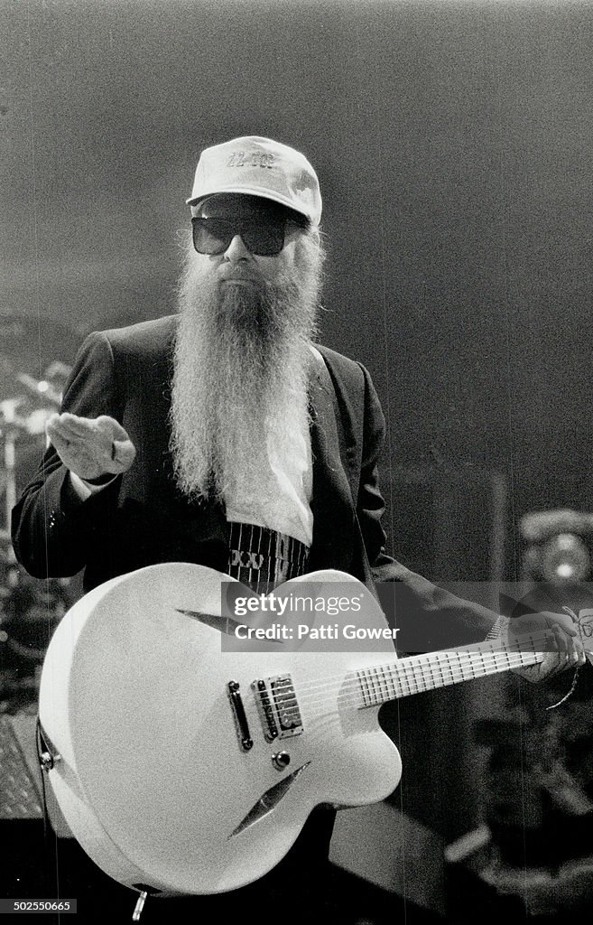 Hairy Godfather of Rock: Billy Gibbons looks sultably goofy in sunglasses; black suit; white guitar;