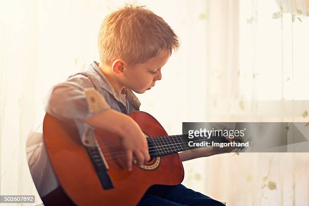 kleine junge üben gitarre. - saiteninstrument spielen stock-fotos und bilder