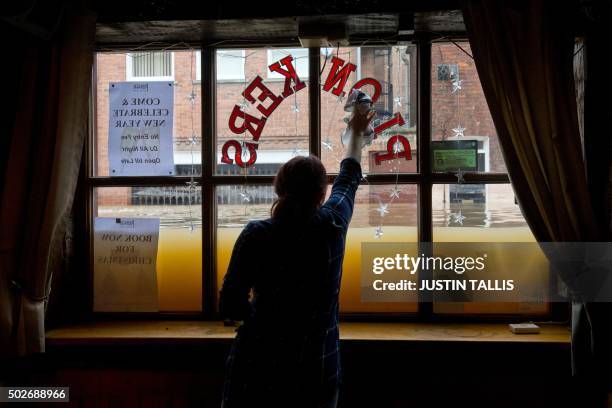Woman cleans the inside window of her wine bar, as the floodwaters rise from the rivers Foss and Ouse, after they burst their banks in York, northern...