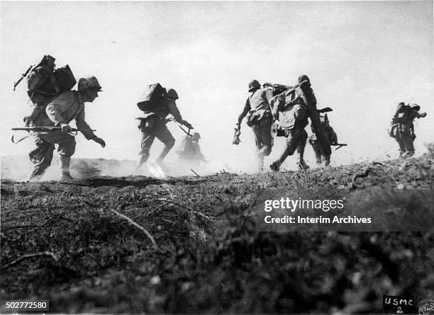 Low-angle view of US Marines, carrying packs and equipment, as they crouch and run towards the cover of smoke during the inland drive, Iwo Jima,...