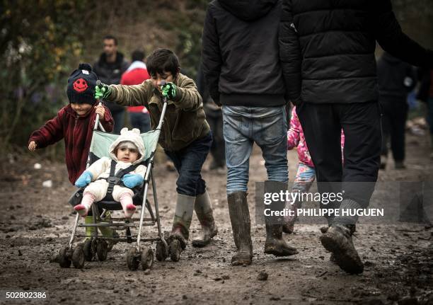 Young migrants or refugees walk with a stroller on December 29, 2015 in a camp in Grande-Synthe. On December 28, 2015 a migrant was found dead in the...