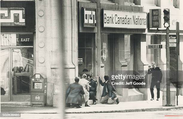 Policemen crouch at door of King and Yonge Sts. Branch of Banque Canadienne Nationale where a gunman is holding hostages. Drama began before noon.