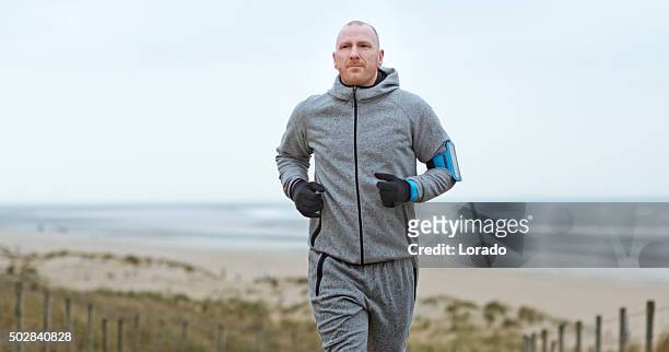 middle aged man jogging on seafront on winter morning - muscle men at beach stockfoto's en -beelden