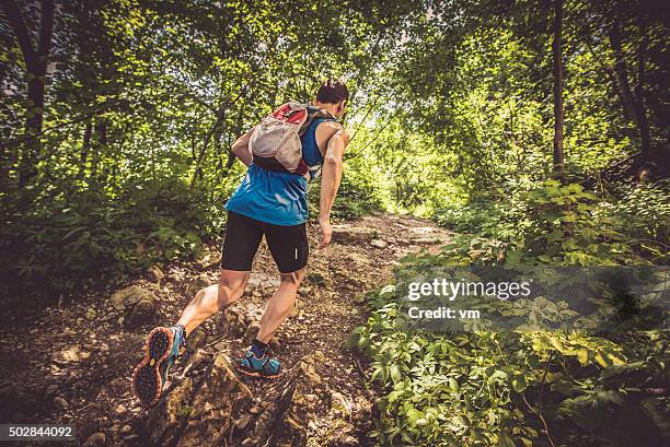 rear view of a man running uphill in a forest - uphill stockfoto's en -beelden