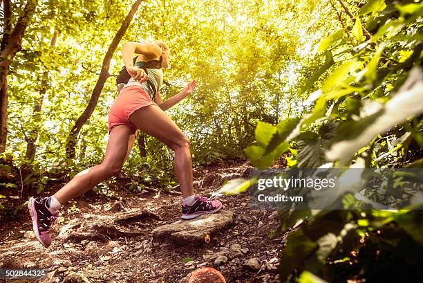 seitenansicht einer frau laufen bergauf in einem wald - trailrunning stock-fotos und bilder