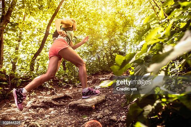 vista lateral de una mujer corriendo en el bosque arriba - carrera de campo través fotografías e imágenes de stock