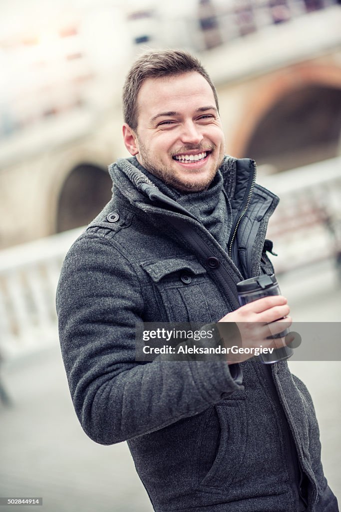 Smiling Young Man with Coffee in Hands on City Street