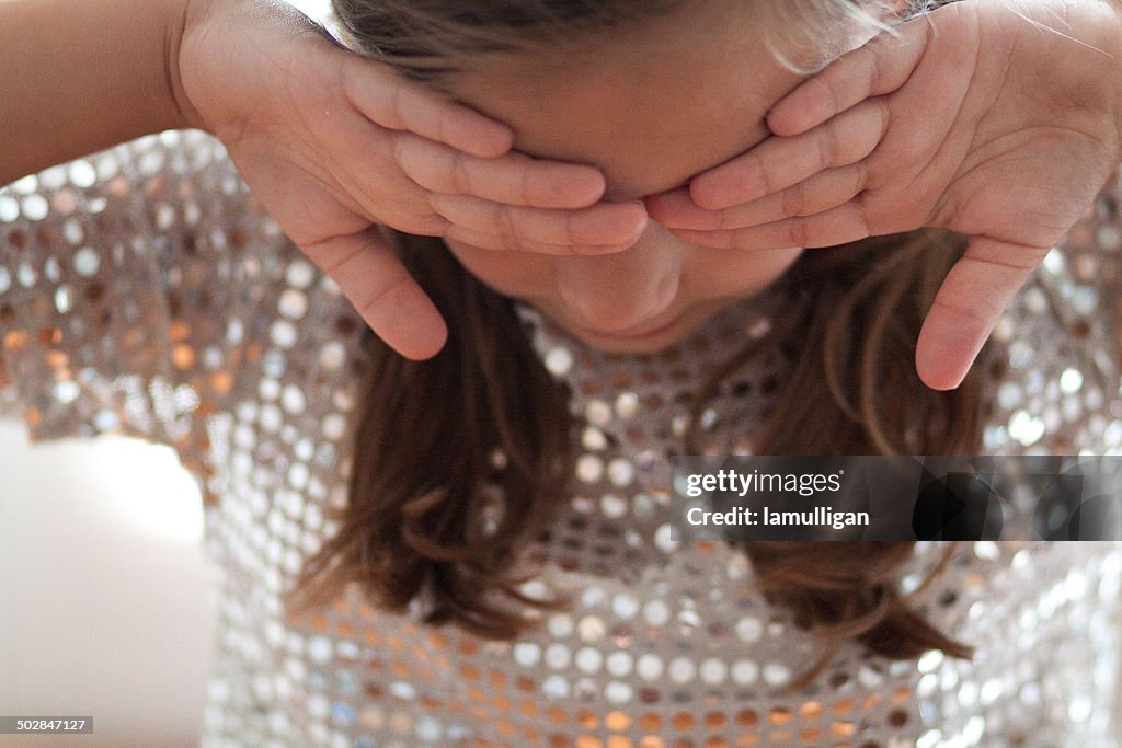 Girl in a sequin top covering eyes with backs of hands