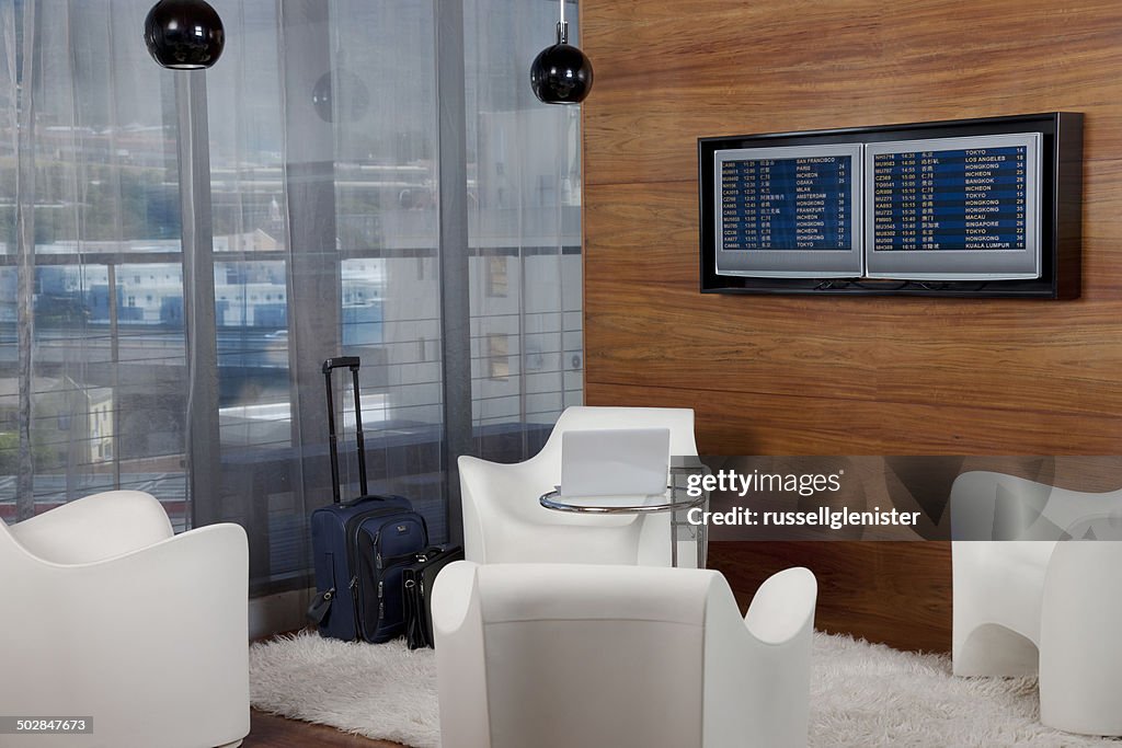 Airport lounge with travel bag, laptop and departure boards